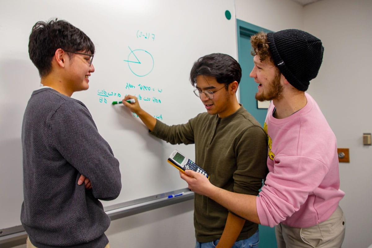 Three San Juan College students working on a math problem on a whiteboard